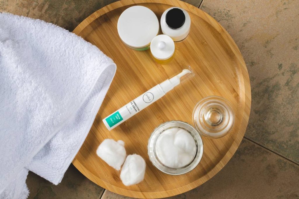Eye cream with cotton buds and wooden tray in bathroom